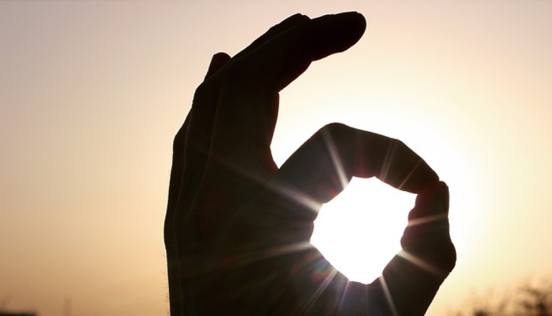 Hand giving "OK" sign in front of the sun